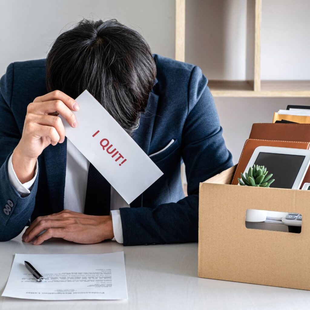 Person with head down and holding a sign that says, "I quit!"
