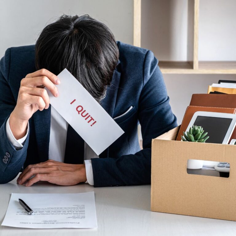 Person with head down and holding a sign that says, "I quit!"