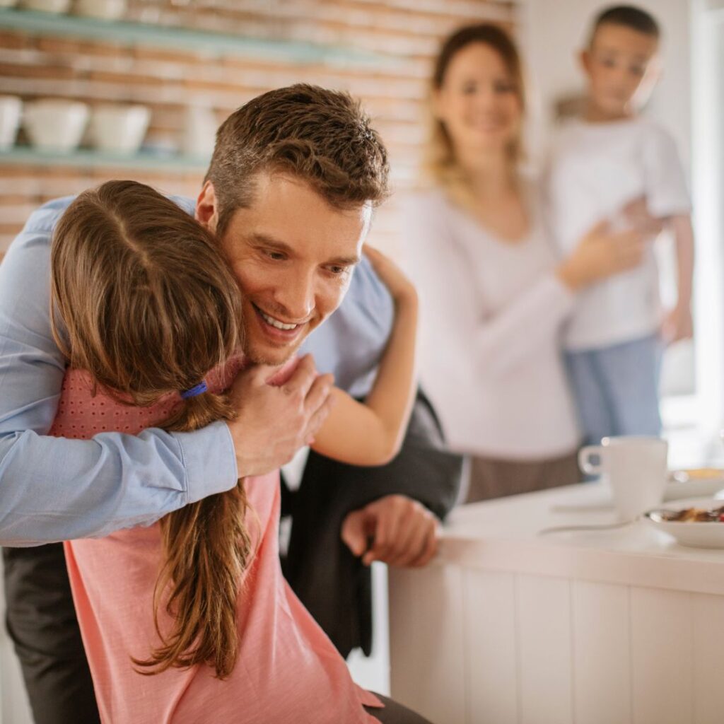 Parent hugging child with another parent and child in the background