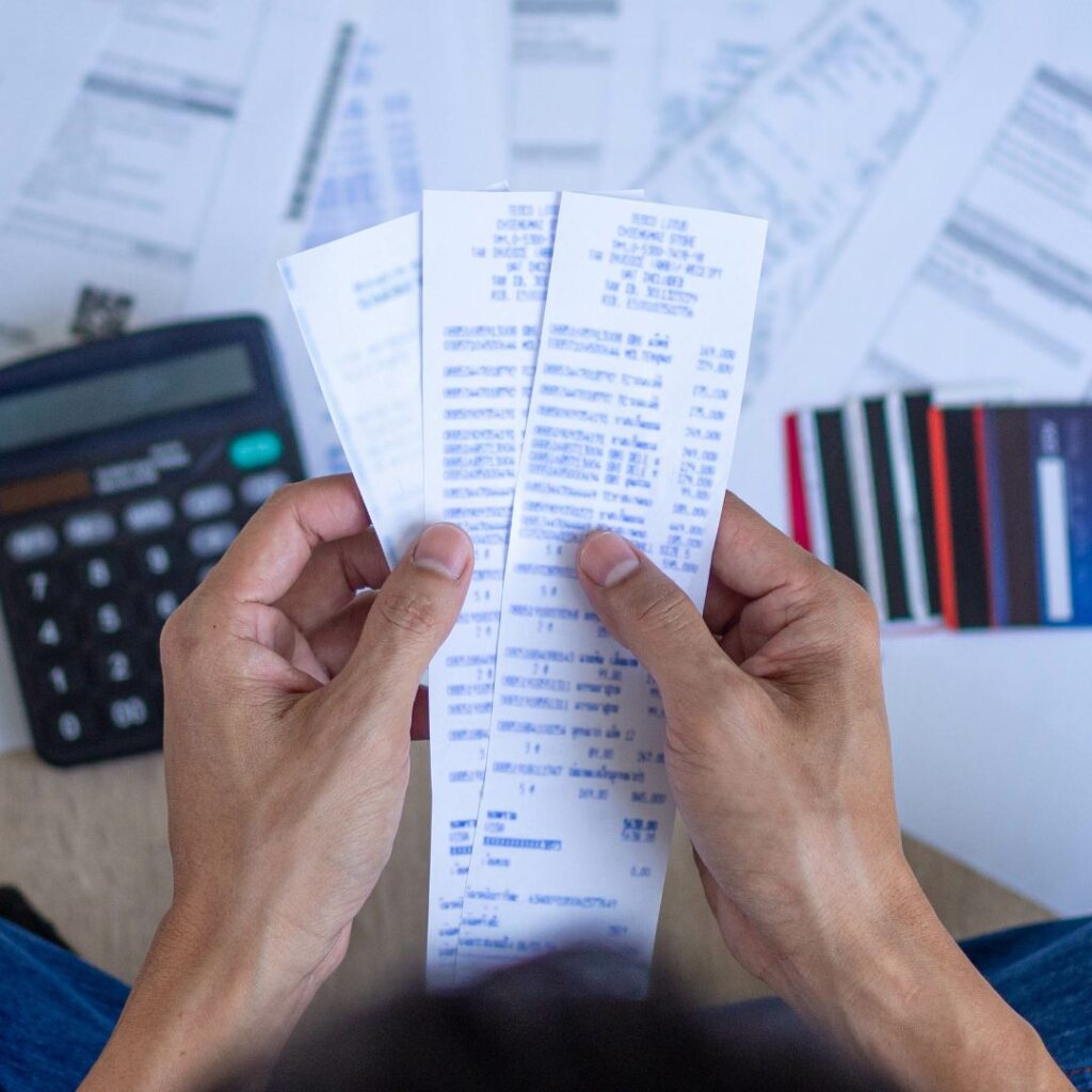 Person's hands holding receipts above a calculator and credit cards; engaged in budgeting