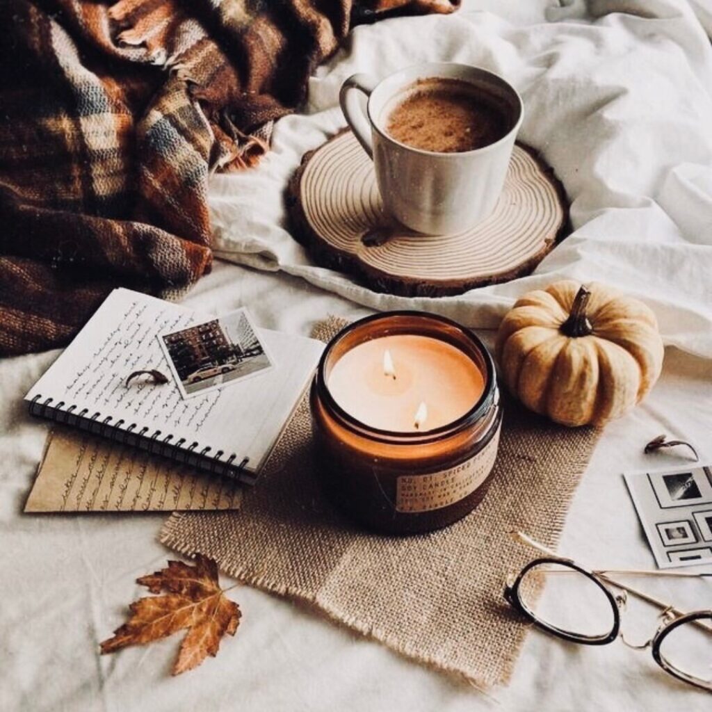 A fall-themed deskscape with a candle, pumpkin, journal, glasses, and cup of coffee.