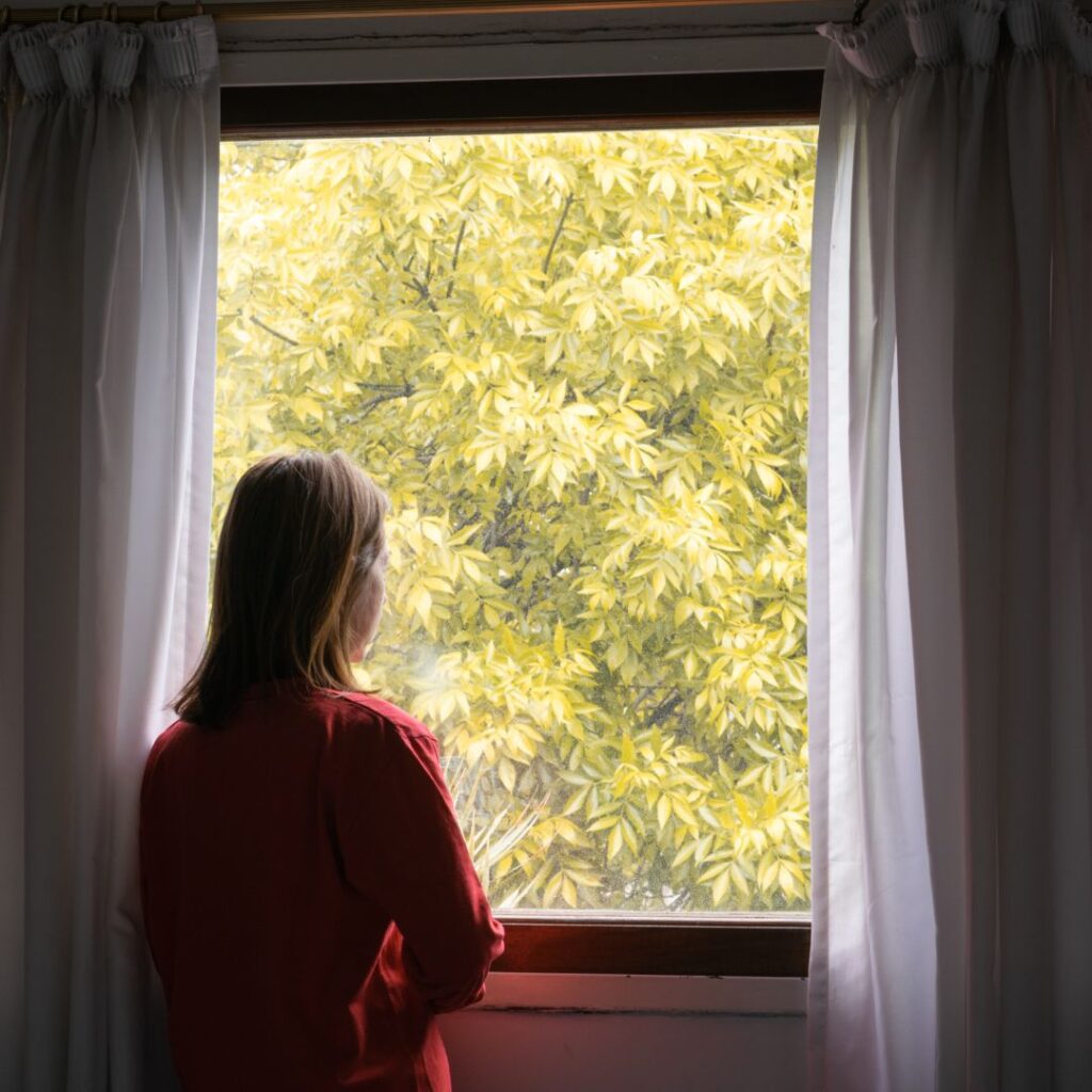 Woman standing in front of a window, looking out.