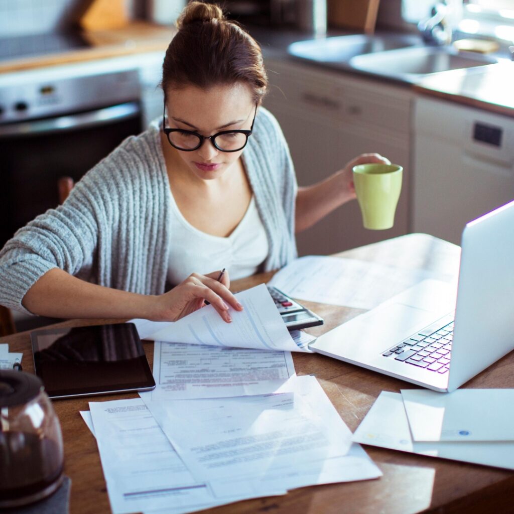 Woman at computer drinking a cup of coffee and reviewing financial documents